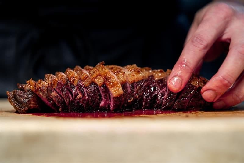 A hand holding a sliced piece of grilled meat
